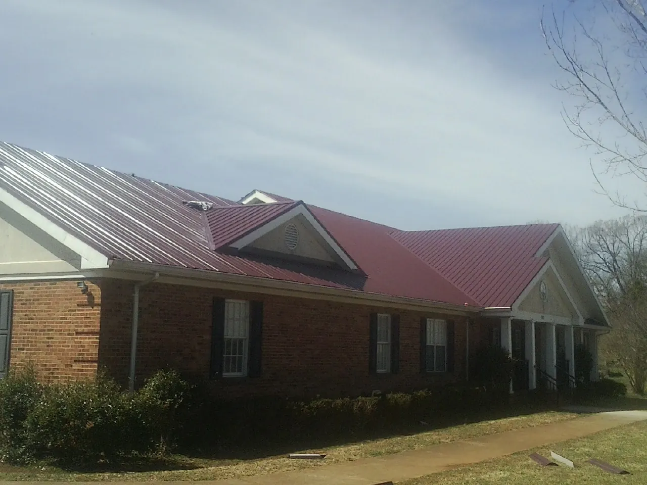 Red metal roof with gabled entries on a long brick building, from a Hail Damage Roof Repair job in Buckland