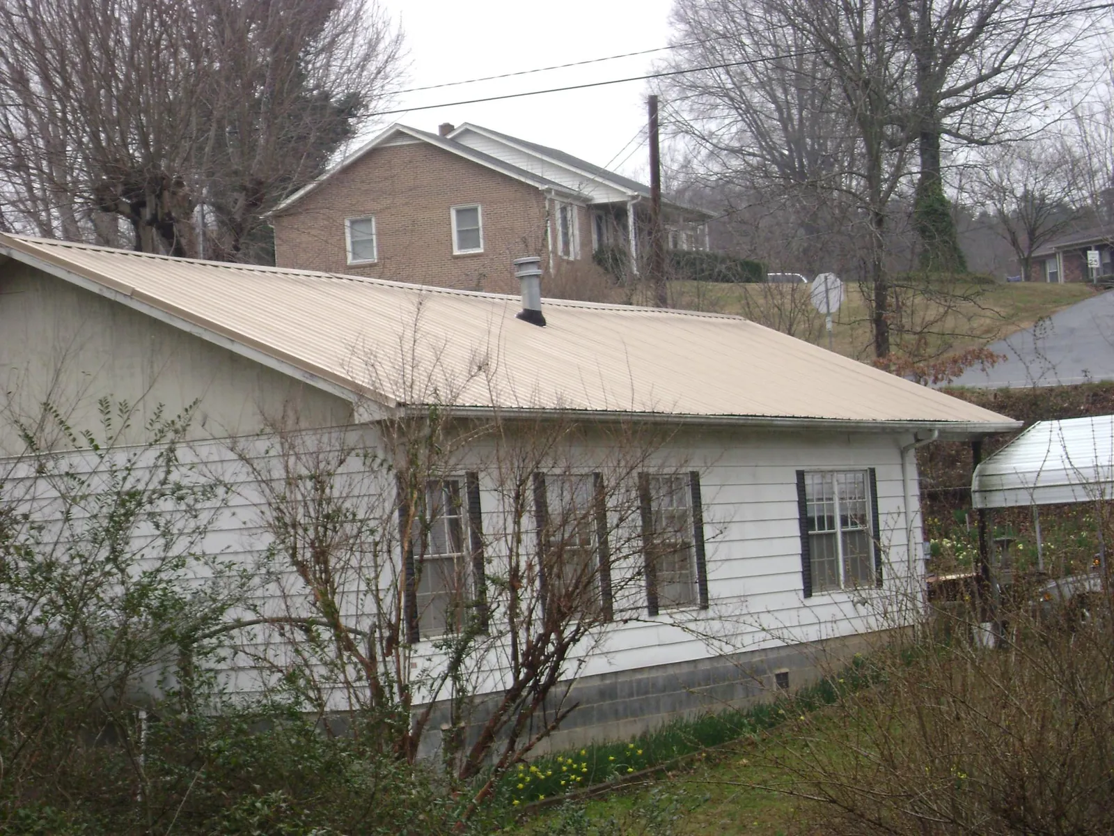 Tan metal roof on a white sided house set into a hillside — Commercial Roofing by Roofing Brothers in Buckland
